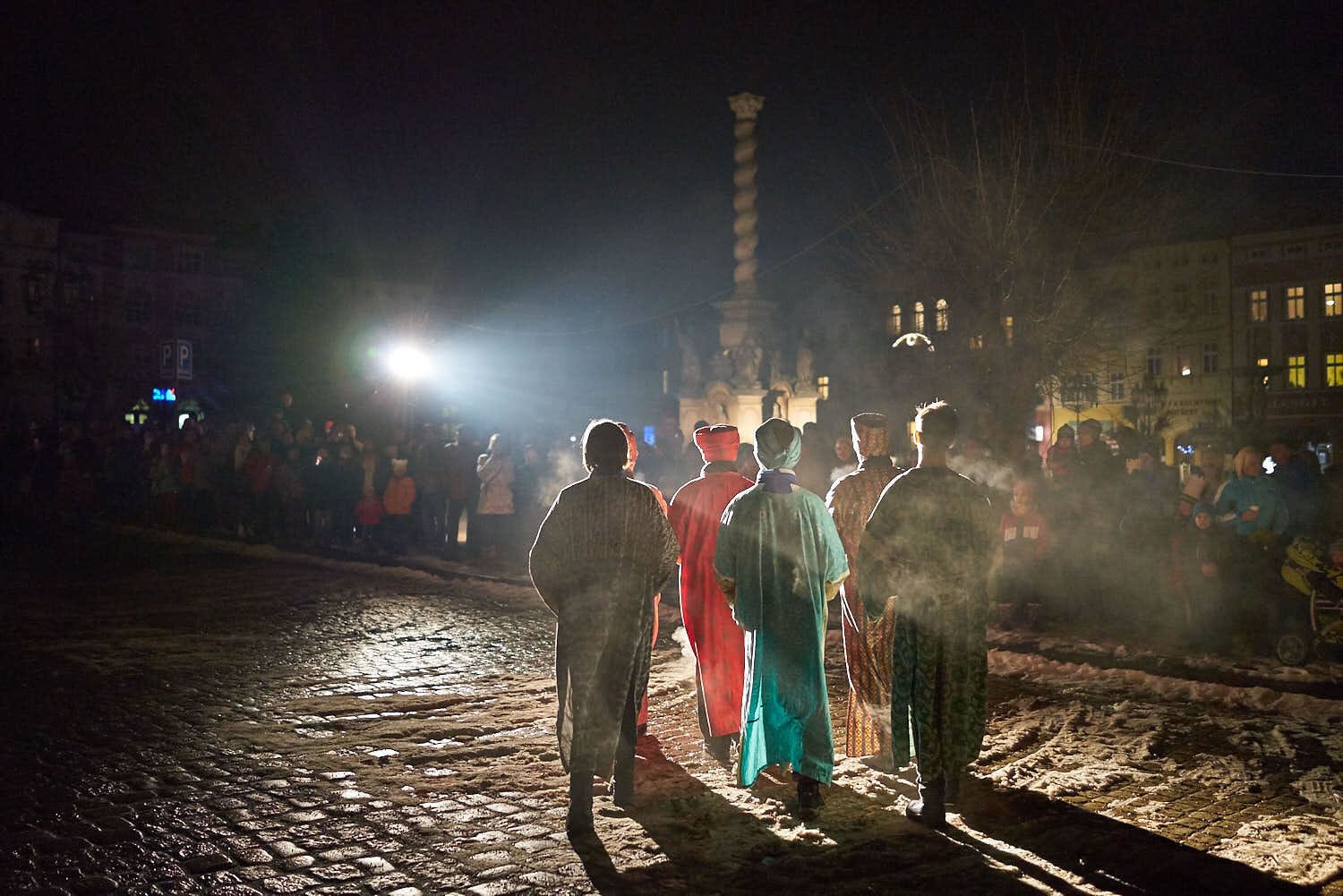 Skupinka dětí v kostýmech, osvícená ve tmě a otočená zády k fotografovi