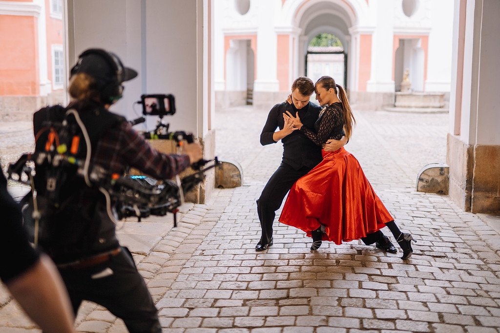 Dva tanečníci na nádvoří broumovského kláštera s kameramanem, který zabírá jejich vystoupení