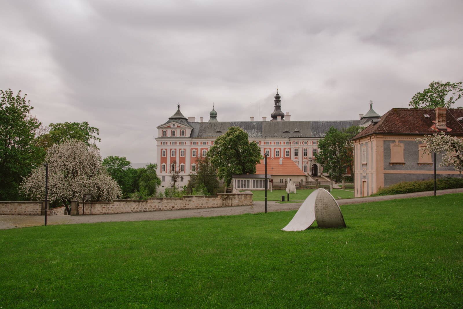 Pohled na Broumovský klášter a klášterní zahradu se sochou v popředí